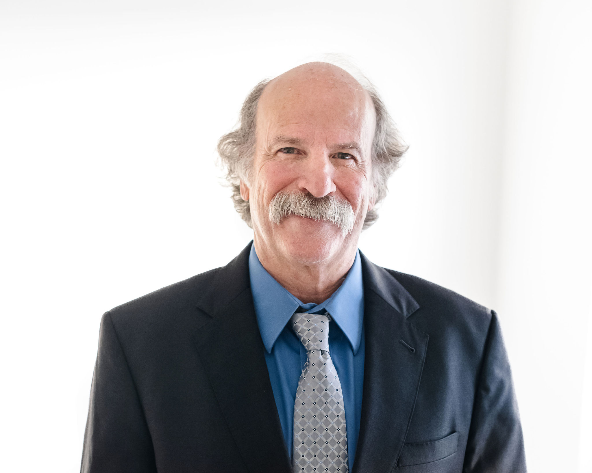 Dr. Roger Light, PhD, ABPP, ABCN, smiling in a suit and tie against a bright background